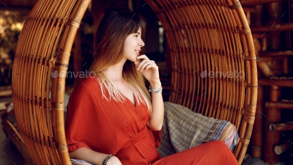 Beautiful woman in orange dress posing in tropical villa.