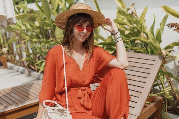female in straw hat and orange playsuit resting on her villa during vacation on Bali.