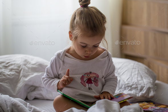 little girl reads a children's book in bed after sleep