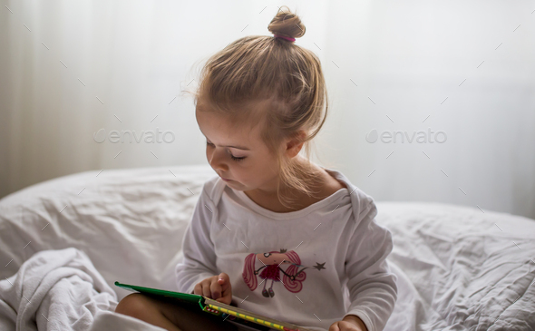 little girl reads a children\'s book in bed after sleep