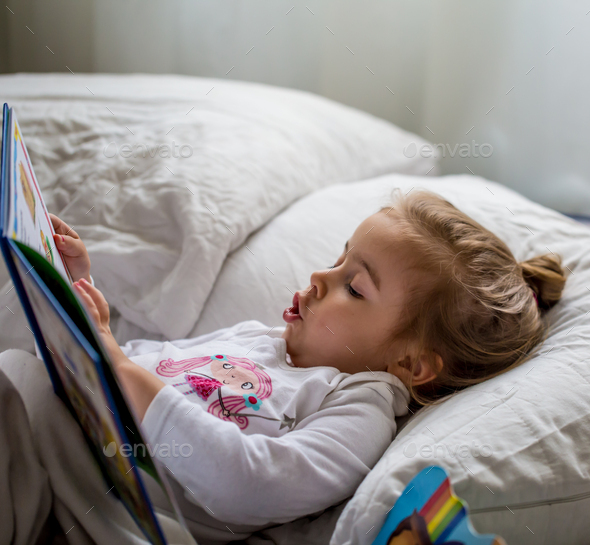 little girl reads a children\'s book in bed after sleep