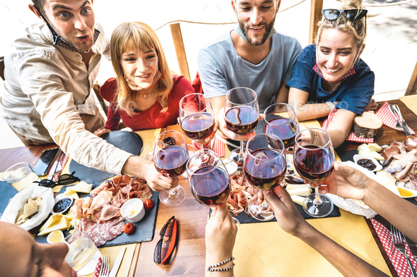 Friends toasting red wine at restaurant bar with open face masks
