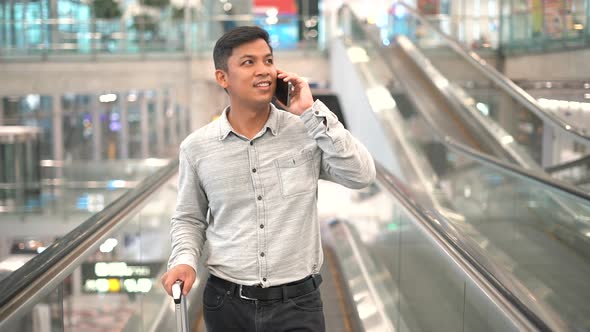 Young man with suitcase standing on the moving walkway while using smartphone