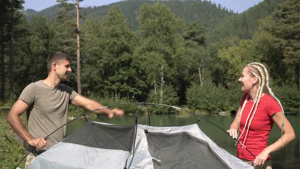 Beautiful Young Couple Man and Woman on a Hike Set Up a Tent in Nature alt