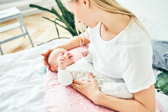 Close up young mother with long blonde hair and a daughter of 2-3 months are resting on the bed