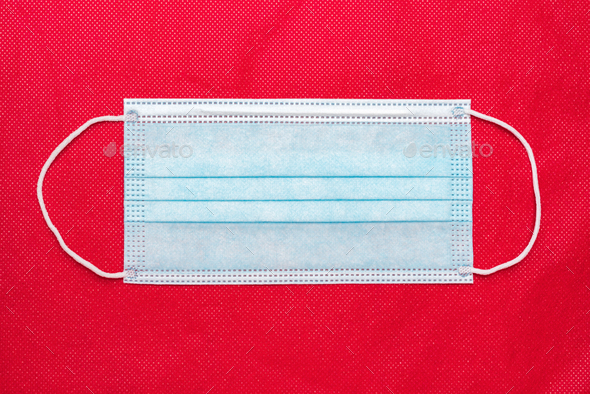 Medical Protective Face Mask on Bright Red Background of Non-Woven Fabric. Concept Global Lockdown