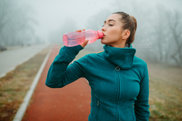 Thirsty young woman drinks water from water bottle as refreshment after  running session. Stock Photo by nebojsa_ki