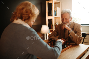 Portrait of smiling elderly couple playing chess at home. It is time for woman to make a move.