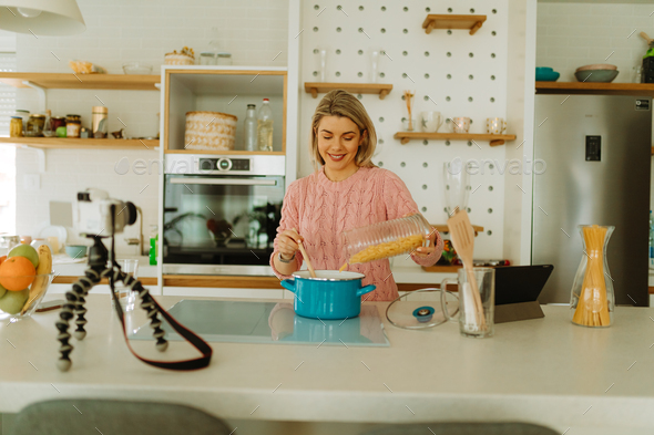 Photo of smiled food blogger preparing pasta while recording video clip for her food blog.