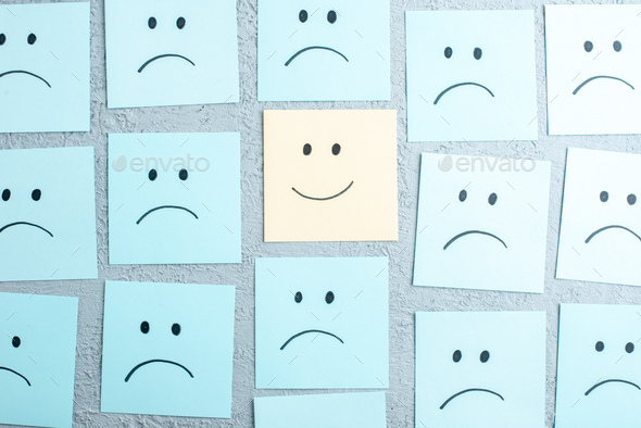 Top view of many sad and happy emoji faces drawings on gray background