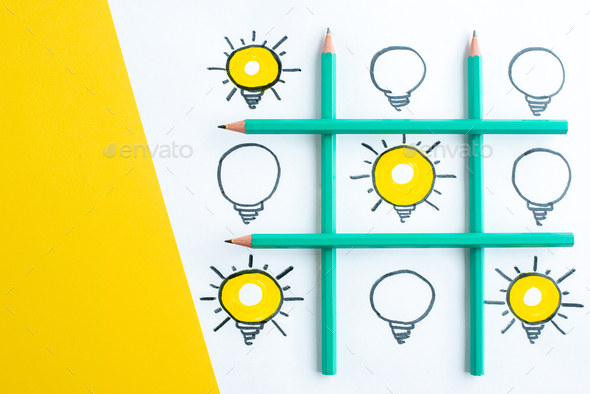 Top view of table arranged with pens with many light bulbs on white blank on yellow background