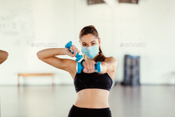 Young woman wear mask and doing exercises with dumbbells