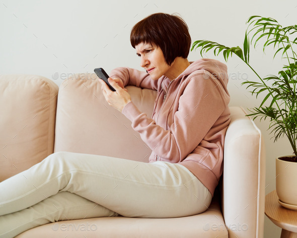 Portrait of mature woman looking on mobile phone with surprise and alarm, confusion and frown