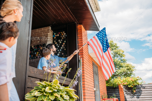 family with american flag standing on country house porch