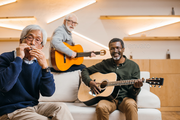 group of smiling senior friends playing music with guitars and harmonica