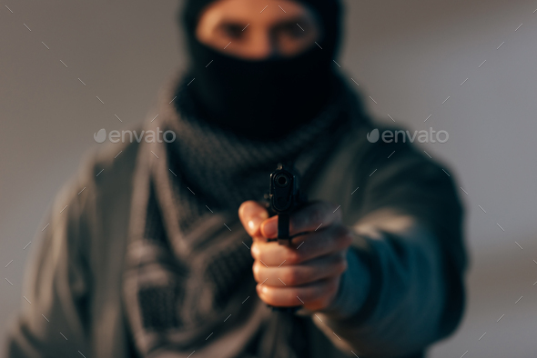 Terrorist in mask and scarf aiming gun at camera