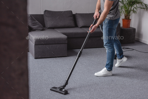 cropped image of man cleaning carpet with vacuum cleaner in living room