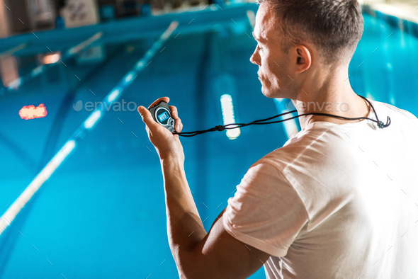 handsome swim trainer with stopwatch standing at competition swimming pool