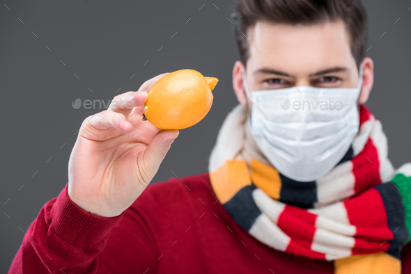 ill man in warm scarf and medical mask holding lemon, isolated on grey