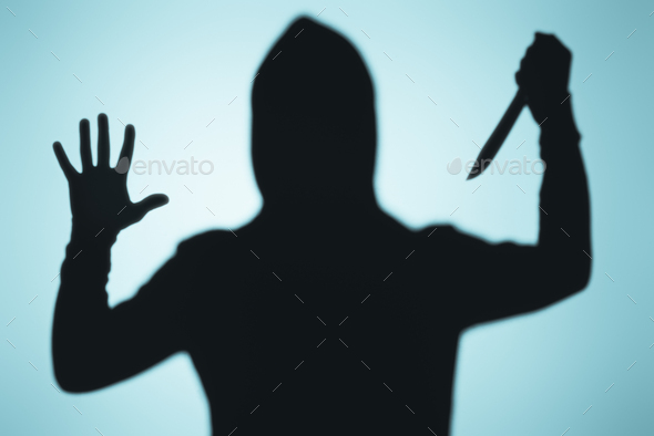 scary shadow of person in hood holding knife on blue