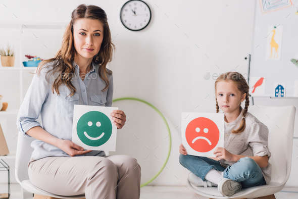 adult psychologist and child holding happy and sad emotion faces cards