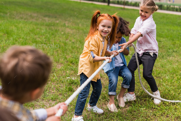 happy beautiful multiethnic kids pulling rope in park