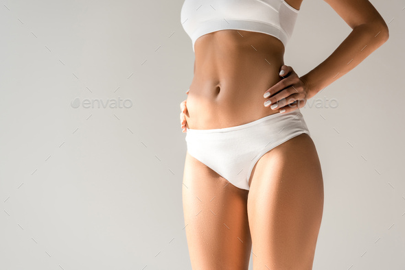 cropped view of slim woman in underwear posing with hands on hips isolated  on grey Stock Photo by LightFieldStudios