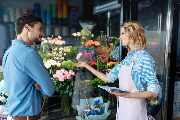 young female florist and handsome male client smiling each other in flower shop