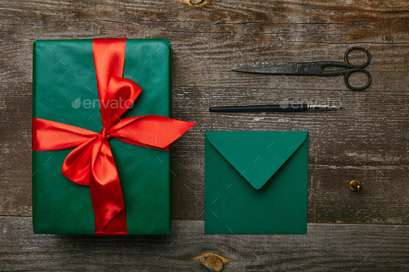 top view of green wrapping paper, scissors and present with red ribbon on  wooden background Stock Photo by LightFieldStudios