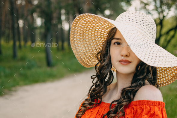 Summer skin hair care, natural beauty, Summer time. Young brunette woman with curly hair in straw