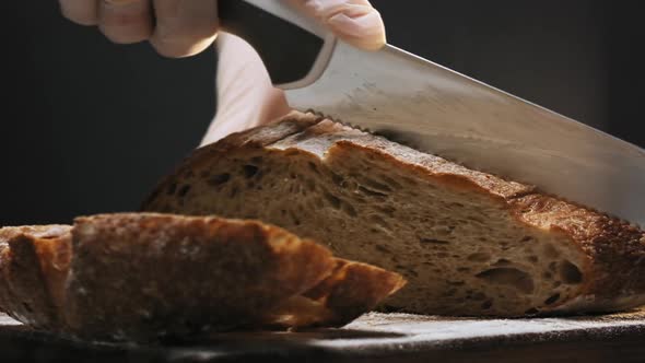 Person in Gloves Cuts Slice of Warm Bread on Wooden Board alt