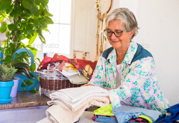 Attractive elderly woman with grey hair busy with houseworks. Ready to iron a lot of clothes