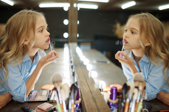 Little girl using lipstick in makeup salon