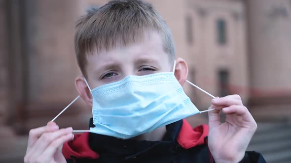 Child Boy Takes Off His Medical Mask Outdoors.