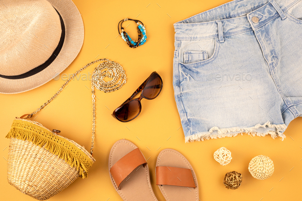 Flat lay with woman fashion accessories, jeans shorts, hat, sunglasses over yellow background