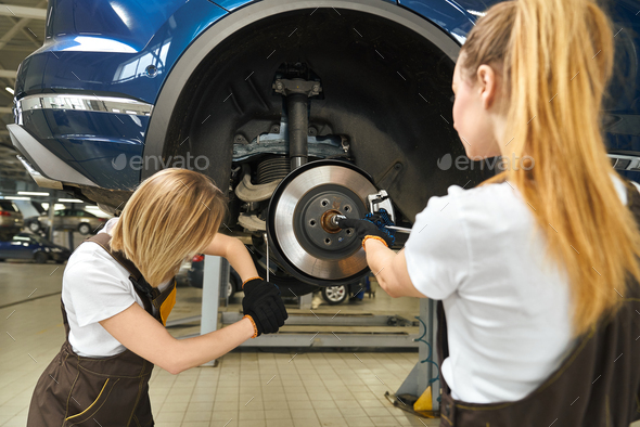 Two female mechanics repairing car brake disc