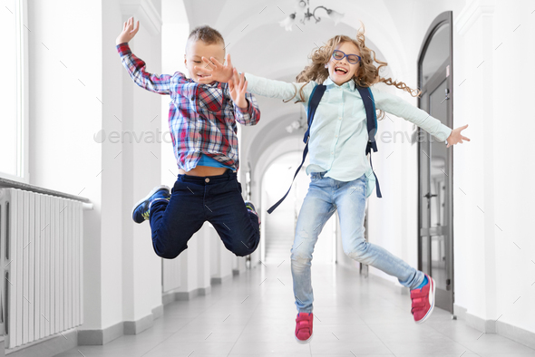 Happy pupils boy and girl high jumping up at school