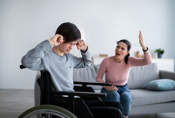 Teenage boy in wheelchair having fight with his angry mom, closing ears not to hear her quarreling