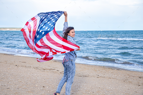 A young woman with an American flag runs by the sea .