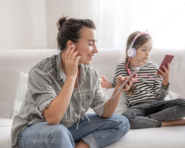 A young mother and her daughter are listening to music on their phones.
