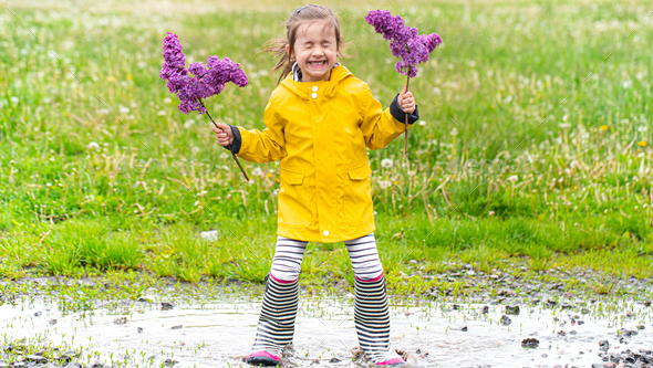 A little girl in rubber boots and flowers in her hands.
