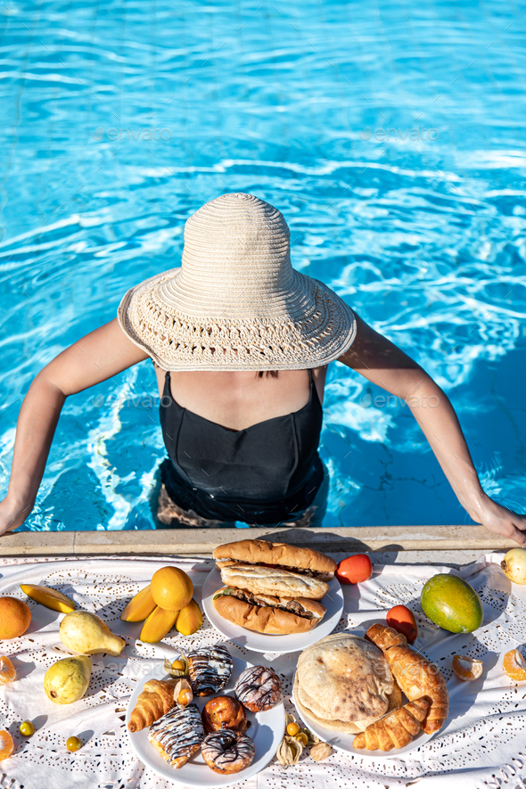 A girl stands in clear blue water in the pool with a delicious breakfast.