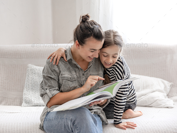 Young mom and daughter have fun together, doing homework with a book and a phone.