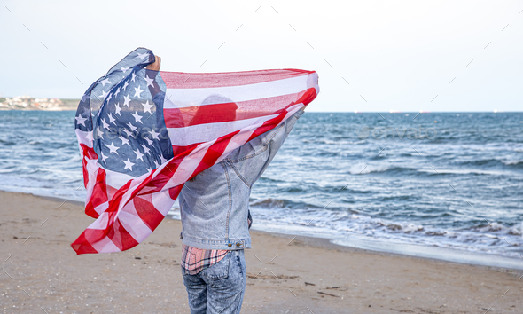 A young woman with an American flag runs by the sea .