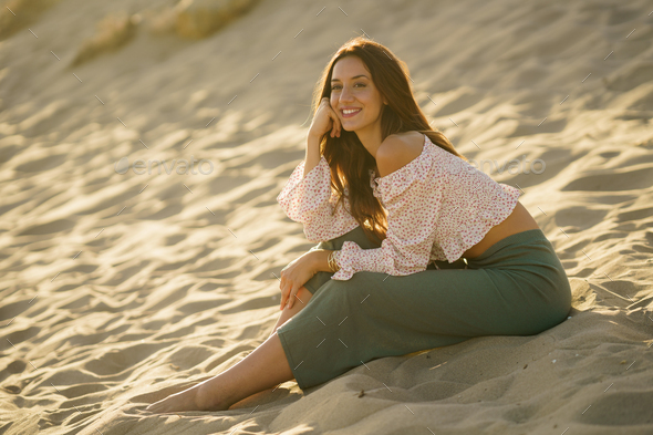 Smiling woman sitting on the sand of the beach