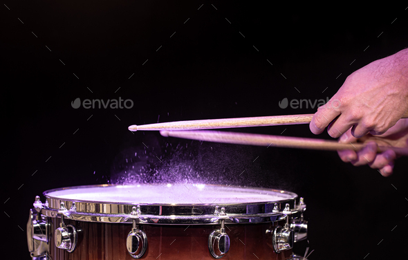 Drum sticks hitting snare drum with splashing water on black background.