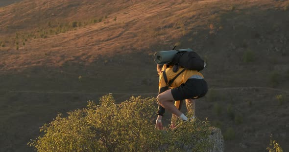 Young Man Traveler with Camera Climbing on the Top of Rock and Looking Into Sunset Male Tourist with alt