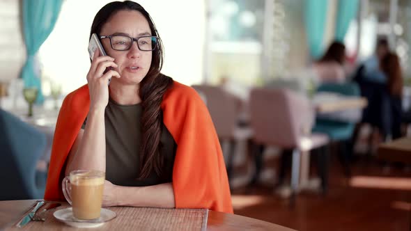 Businesswoman is Calling By Mobile Phone During Coffee Break in Cafe Resting with Cup of Latte alt