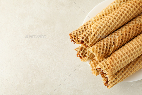 Plate with wafer rolls with condensed milk on white textured background
