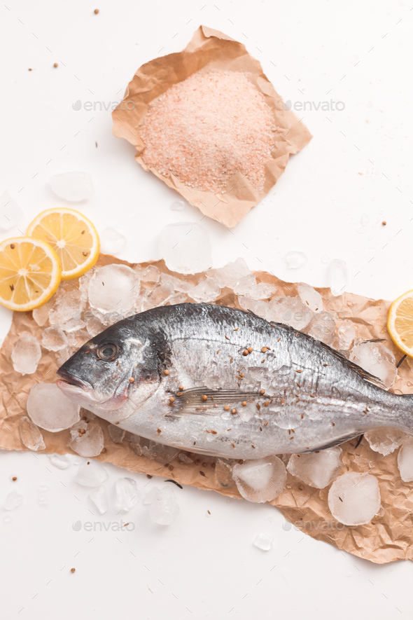 Raw dorada fish or gilt-head bream on ice with lemon and salt over white background - Stock Photo - Images